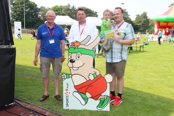 Maskottchen „Hermi" wirbt für Sport im Verein: (von links) Karl-Heinz Danger, Frank Hilker und Michael Peuker mit Sohn Jonathan präsentieren den „Sports4kids"-Gutschein. - © Lorraine Brinkmann