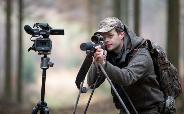 Der Jäger Rouven Kreienmeier steht mit Büchse und Filmkamera in einem Waldstück von einem Jagdrevier. - © Friso Gentsch/dpa