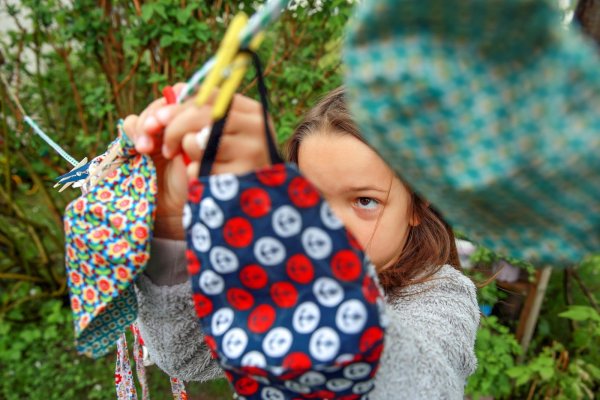 Ein Mädchen hängt im Garten gewaschene Mund-Nasen-Masken auf. - © picture alliance / dpa-tmn