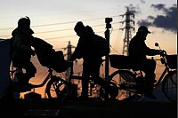 Schattenrisse: Menschen fahren in der Abenddämmerung in Yokohama in der Nähe von Tokio mit Fahrrädern im Gegenlicht der Abendsonne. - © Eugene Hoshiko/AP/dpa