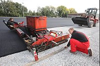 Letzte Arbeiten auf dem Jerxer Sportplatz: Mit einem Kunststofffertiger bringen die Sportstättenbauer Michael Roschnow (links) und Holger Friederichs (vorn) eine wasserdurchlässige Elastikschicht aus polyurethan-gebundenem Gummigranulat auf. - © Foto: Preuss