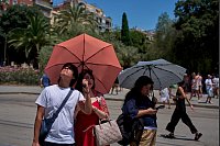 Touristen schützen sich amvor der Kirche Sagrada Familia mit Regenschirmen vor der Sonne. - © Emilio Morenatti/AP/dpa
