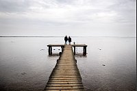 Zweisamkeit: Ein Paar geht bei trübem Wetter über einen Holzsteg am Jadebusen im niedersächsischen Dangast. - © Hauke-Christian Dittrich/dpa