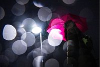 Lichtspiel in der Dunkelheit: Eine Frau mit Regenschirm geht am frühen Morgen in Bremen über eine Brücke über die Weser. - © Sina Schuldt/dpa