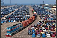 Außenhandel China - Ein Güterzug fährt in der ostchinesischen Provinz Shandong an neuen Autos vorbei, die in einem Hafen auf ihre Verschiffung warten. - © Uncredited/CHINATOPIX/AP/dpa