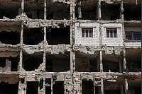 Die Wände und Fenster einer kürzlich restaurierten Wohnung ragen aus einem beschädigten Wohnhaus im vom Krieg zerstörten Viertel Al-Waer heraus. - © Ghaith Alsayed/AP/dpa