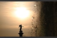Die Sonne geht vor der Jubiläumssäule auf dem Schlossplatz unter, rechts die Fontäne eines Wasserspiels. - © Bernd Weißbrod/dpa