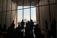 Besucher stehen vor einem Fenster mit Blick auf die Pyramiden von Gizeh im Großen Ägyptischen Museum (GEM). - © Gehad Hamdy/dpa