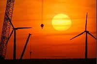 Sonnenaufgang über einer Landschaft mit Windenergieanlagen und einem Kran auf einer Baustelle für ein neues Windrad in Brandenburg. - © Patrick Pleul/dpa