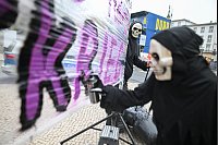 Protestaktion gegen Krieg: Eine Frau mit einer Totenkopfmaske sprüht während einer Aktion vor der russischen Botschaft gegen den russischen Angriffskrieg in der Ukraine eine Parole auf ein Transparent. - © Sebastian Christoph Gollnow/dpa