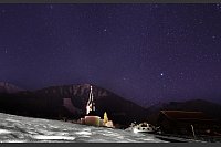 Die Pfarrkirche Mariä Opferung steht in Riezlern unter dem Sternenhimmel hinter einer schneebedeckten Wiese. - © Karl-Josef Hildenbrand/dpa