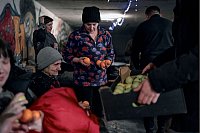 Ein Polizist in Awdijiwka beschenkt Menschen mit Mandarinen und Äpfeln in der Vorweihnachtszeit in einem als Bunker genutzten Keller eines Wohnhauses. - © Libkos/AP/dpa