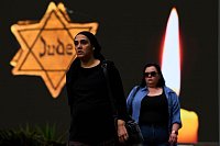 Holocaust-Gedenktag in Israel: Zwei Frauen gehen neben einer Plakatwand mit der Abbildung eines gelben Davidsterns, auf dem das Wort «Jude» steht, entlang. - © Oded Balilty/AP/dpa