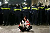 Eine Demonstrantin sitzt während der Proteste in Georgien vor Polizisten. - © Zurab Tsertsvadze/AP/dpa