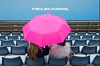 Zuschauerinnen sitzen während einer Regenunterbrechung bei den Australian Open mit einem Regenschirm auf der Tribüne. - © Frank Molter/dpa