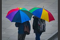 Unter bunten Regenschirmen suchen zwei Passanten Schutz vor leichtem Regen in der Potsdamer Innenstadt. - © Soeren Stache/dpa
