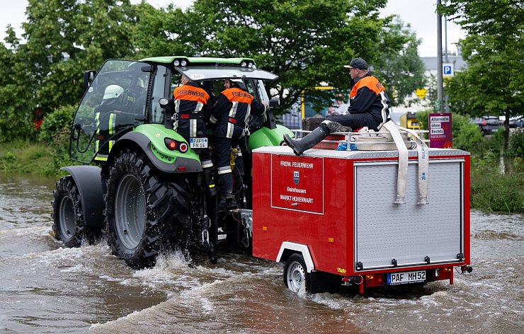 Feuerwehrleute fahren in Reichertshofen über einr überflutete Straße. - © Sven Hoppe/dpa