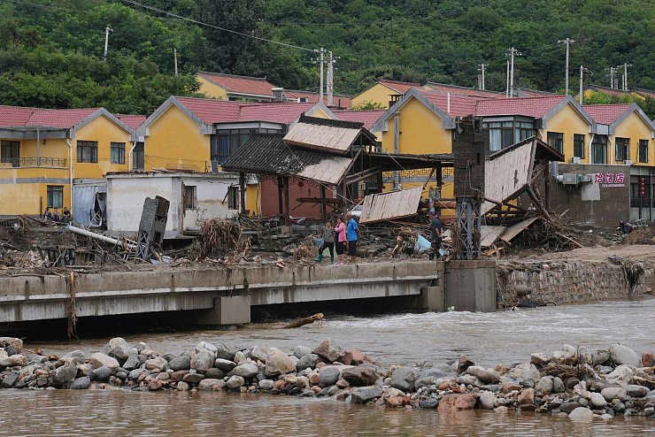 Dorfbewohner versammeln sich in der Nähe einer Brücke, die nach schweren Regenfällen im Bezirk Miyun am Stadtrand von Peking überflutet wurde. - © Andy Wong/AP/dpa