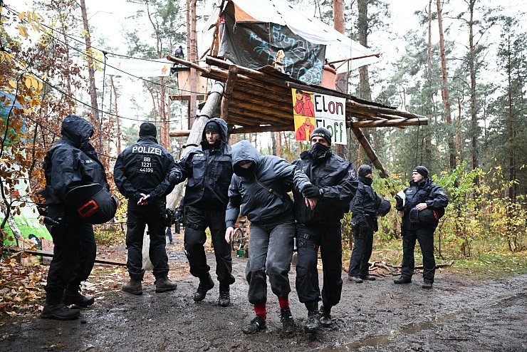 Ein Aktivist wird von Polizisten aus dem Protestcamp in der Nähe des Tesla-Autowerks in Grünheide abgeführt. - © Sebastian Christoph Gollnow/dpa