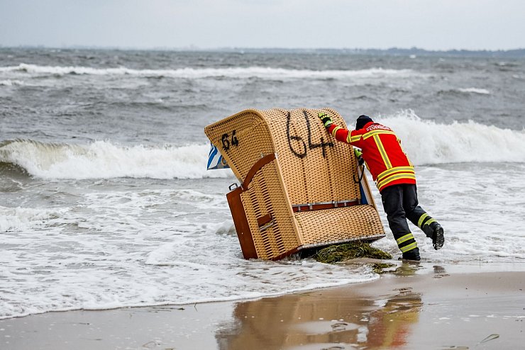 Ein Feuerwehrmann versucht, in Kiel-Schilksee einen Strandkorb vor den Flutwellen der Ostsee zu sichern. - © Axel Heimken/dpa