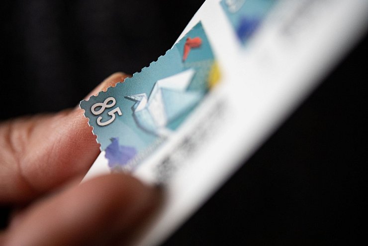 Eine Frau löst eine Briefmarke von einem Briefmarken-Bogen, um sie auf einen Brief zu kleben. - © Marijan Murat/dpa