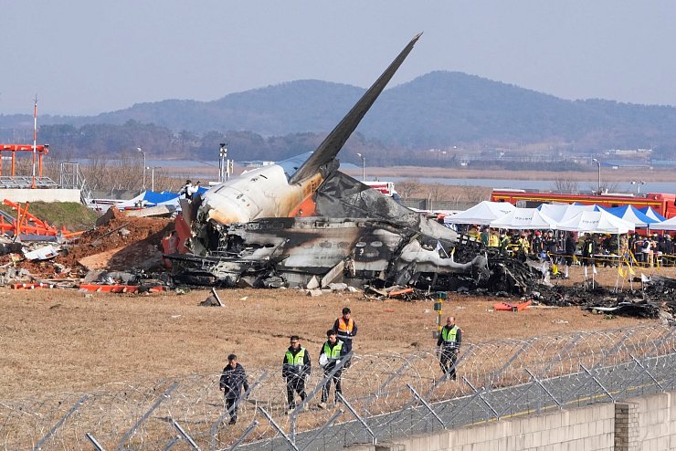 Feuerwehrleute und Rettungskräfte bergen die Opfer des verunglückten Flugzeugs auf dem internationalen Flughafen von Muan. - © Ahn Young-joon/AP/dpa