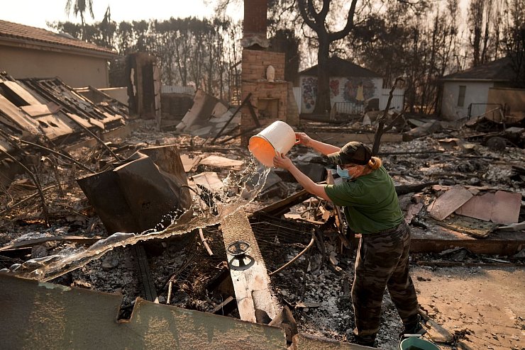 Nancy Belanger gießt Wasser auf das vom Feuer verwüstete Grundstück eines Nachbarn im Stadtteil Pacific Palisades von Los Angeles. - © Jae C. Hong/AP/dpa