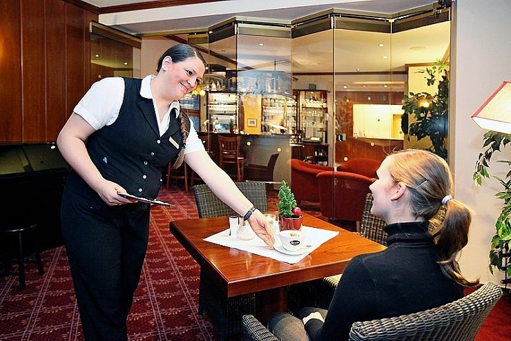Ein Lächeln gehört dazu: Christin Kirsche ist jetzt fest im Team des Ringhotels Bärenstein. Für unser Foto serviert sie Melanie Koszolko (Empfangsleiterin) einen Milchkaffee. - © Foto: Preuss