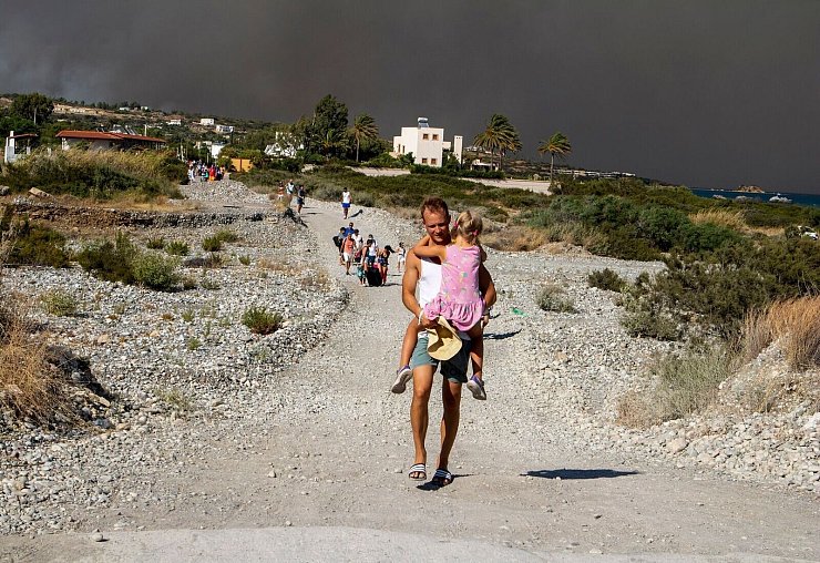Ein Mann mit einem Kind auf dem Arm verlässt ein Waldbrandgebiet auf Rhodos. - © Lefteris Damianidis/InTime News/AP/dpa