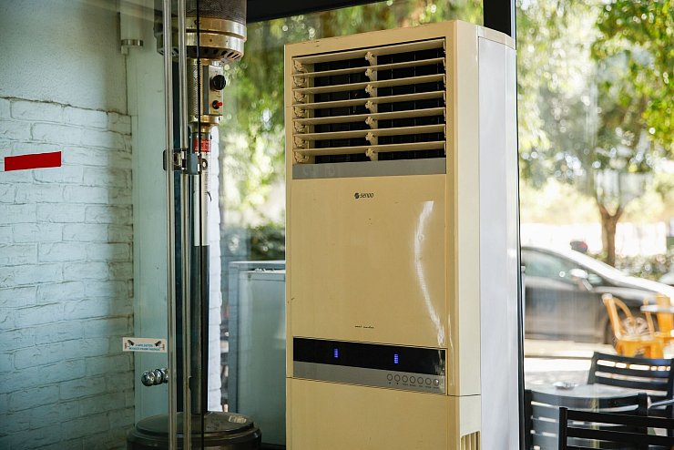 Athen: Eine mobile Klimaanlage steht im verglasten Innenraum eines Cafés. (Archivbild) - © Socrates Baltagiannis/dpa