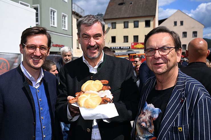 Markus Söder (M.) hält Bratwurst-Semmeln in die Kamera. - © Felix Hörhager/dpa