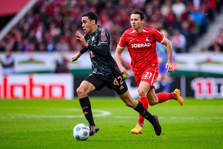 Bayern-Star Jamal Musiala enteilt Freiburgs Nicolas Höfler. - © Tom Weller/dpa