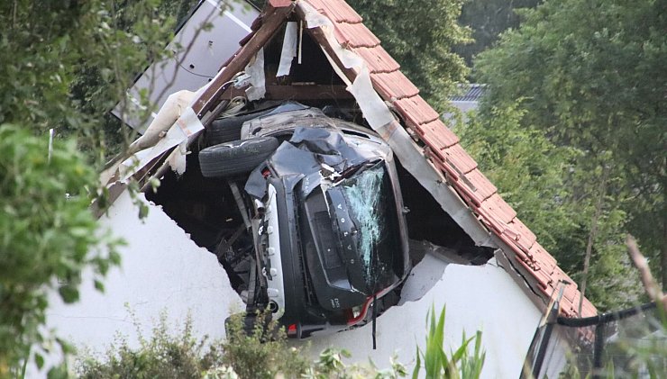 Das Auto liegt nach einem kurzen Flug seitlich in der Mauer einer Scheune. - © -/Moonshine Media/dpa