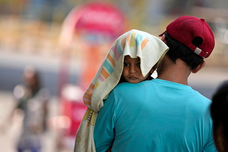 Ein Mann trägt ein Kind, dessen Kopf mit einem Handtuch bedeckt ist. - © Channi Anand/AP/dpa