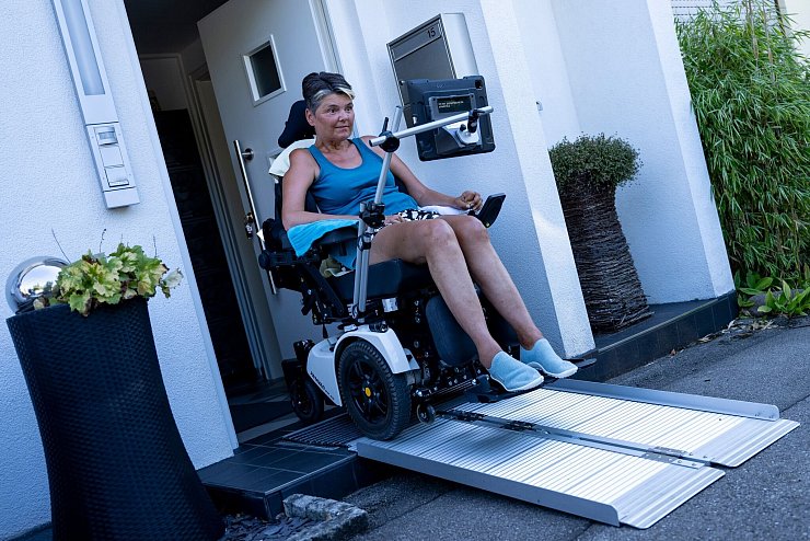 Gabriele Engel fährt mit ihrem Rollstuhl über eine Rampe aus ihrem Haus. - © Lennart Preiss/dpa