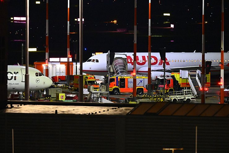 Fahrzeuge der Feuerwehr und ein Krankenwagen stehen am Flughafen vor einem Flugzeug. - © Jonas Walzberg/dpa