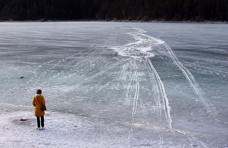 Eine Frau steht am Ufer des zugefrorenen Eibsees, nahe der Stelle an der am Nachmittag mehrere Menschen im Eis eingebrochen waren. - © Karl-Josef Hildenbrand/dpa