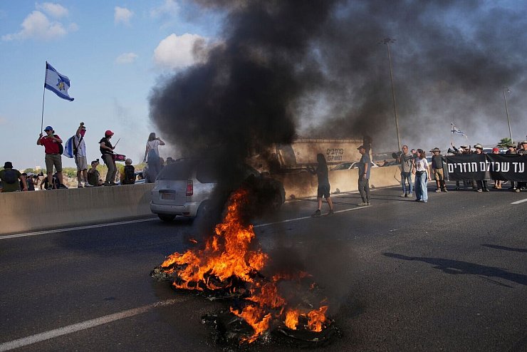 Israelische Demonstranten blockieren eine Straße bei einem Protest. - © Ohad Zwigenberg/AP/dpa