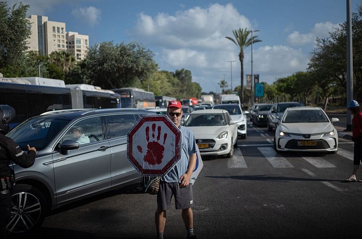 Ein israelischer Demonstrant geht mit einem Schild auf einer Straße, während Autos sich stauen. - © ILIA YEFIMOVICH/dpa