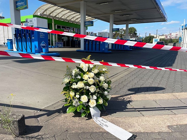 Ein großer Blumenkranz steht vor der überfallenen Tankstelle. - © Christian Schultz/dpa