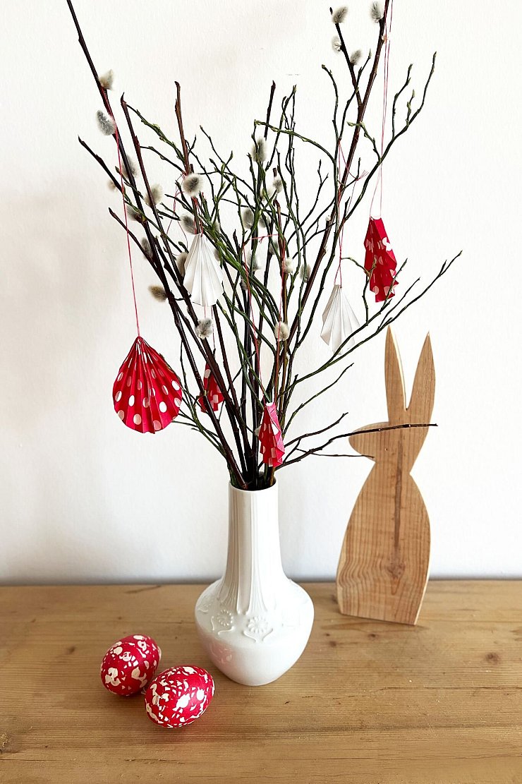 Selbstgemachter Osterschmuck: Aus buntem, gefaltetem Papier werden Anhänger für den Osterstrauß. - © DIY Academy/dpa-tmn
