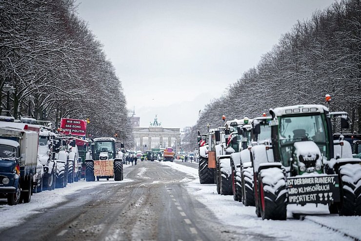 Zahlreiche schneebedeckte Traktoren stehen auf der Straße des 17. Juni vor dem Brandenburger Tor in Berlin. - © Kay Nietfeld/dpa