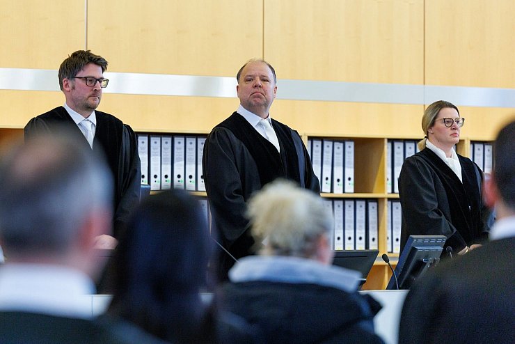Zum Prozessbeginn stehen die drei Richter im Verhandlungssaal. - © Christoph Reichwein/dpa