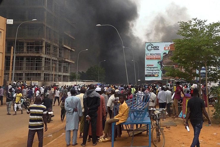 Mit dem brennenden Hauptquartier der Regierungspartei im Rücken demonstrieren Anhänger meuternder Soldaten in der Hauptstadt Niamey. - © Fatahoulaye Hassane Midou/AP/dpa