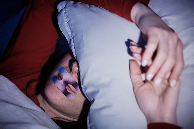 Eine Frau liegt mit einem Mundpflaster im Bett. Ob es hilft? (Illustration) - © Christoph Soeder/dpa