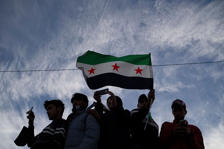 Syrer versammeln sich mit einer Fahne der syrischen Opposition in Damaskus. - © Leo Correa/AP/dpa