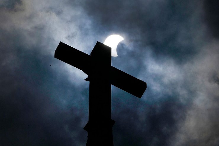 Wolken lösen sich auf und geben über dem Kreuz eines Kirchturms in Manor (Texas) den Blick auf die beginnende Sonnenfinsternis frei. - © Charles Rex Arbogast/AP