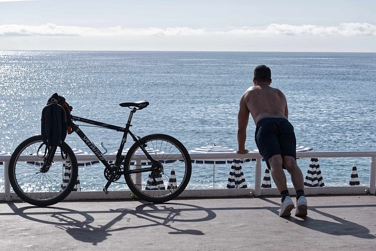 Ein Mann mit nacktem Oberkörper macht am Strand von Nizza neben seinem Fahrrad Übungen. (Archivbild) - © Serge Haouzi/XinHua/dpa