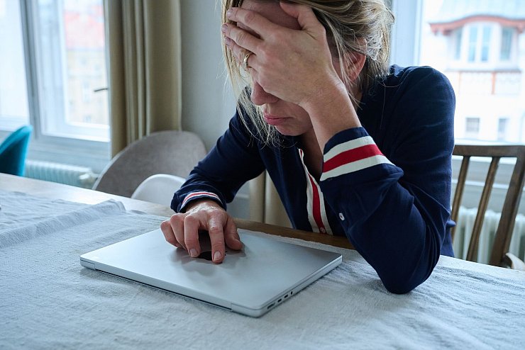 Eine Frau sitzt vor einem geschlossenen Laptop und seufzt. - © Annette Riedl/dpa