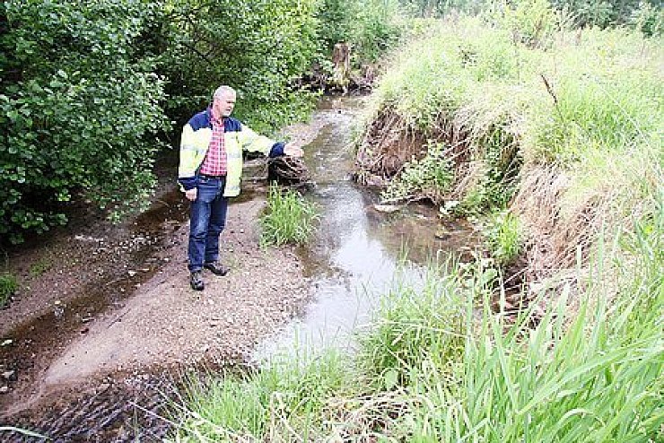 An der Windwehe: Der Gewässerschutzbeauftragte der Gemeinde, Reiner Loer, zeigt auf den Steilabbruch, der sich durch Anlage des Strömungslenkers eigendymnamisch gebildet hat. Foto: Breder